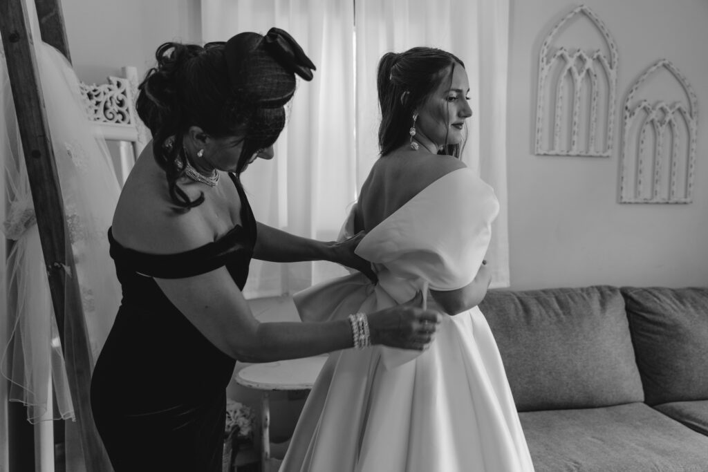 Mother of bride helps bride get zipped into her wedding dress