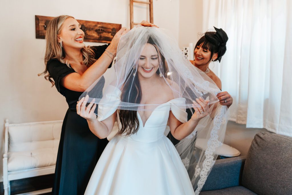 Bride's mother and sister help her put on her wedding day veil