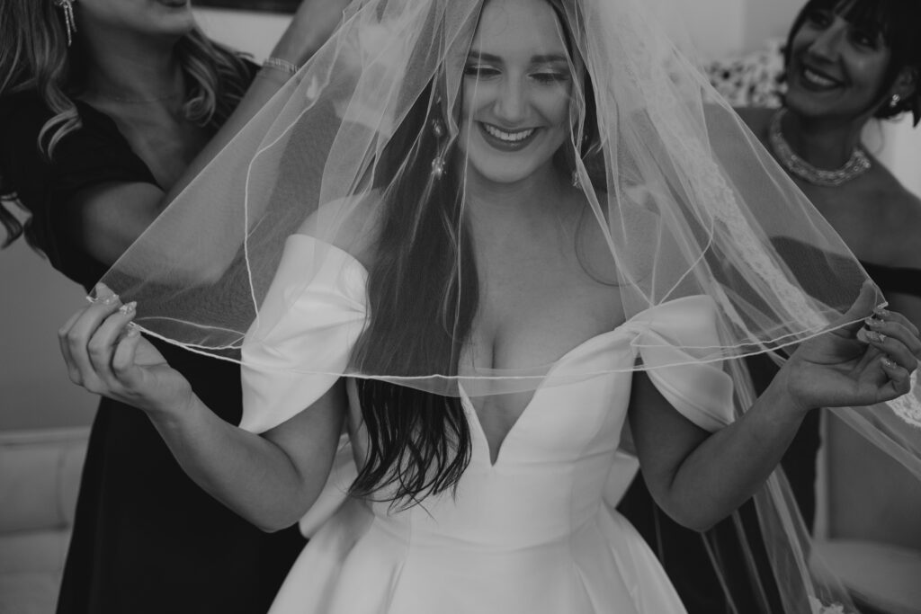 Black and white image of Bride's mother and sister help her put on her wedding day veil